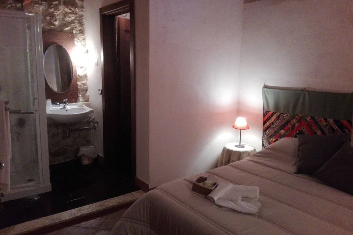 Une chambre à coucher comprenant un lit, une table de chevet, une lampe, ainsi qu’une salle de bain avec un lavabo et un miroir.