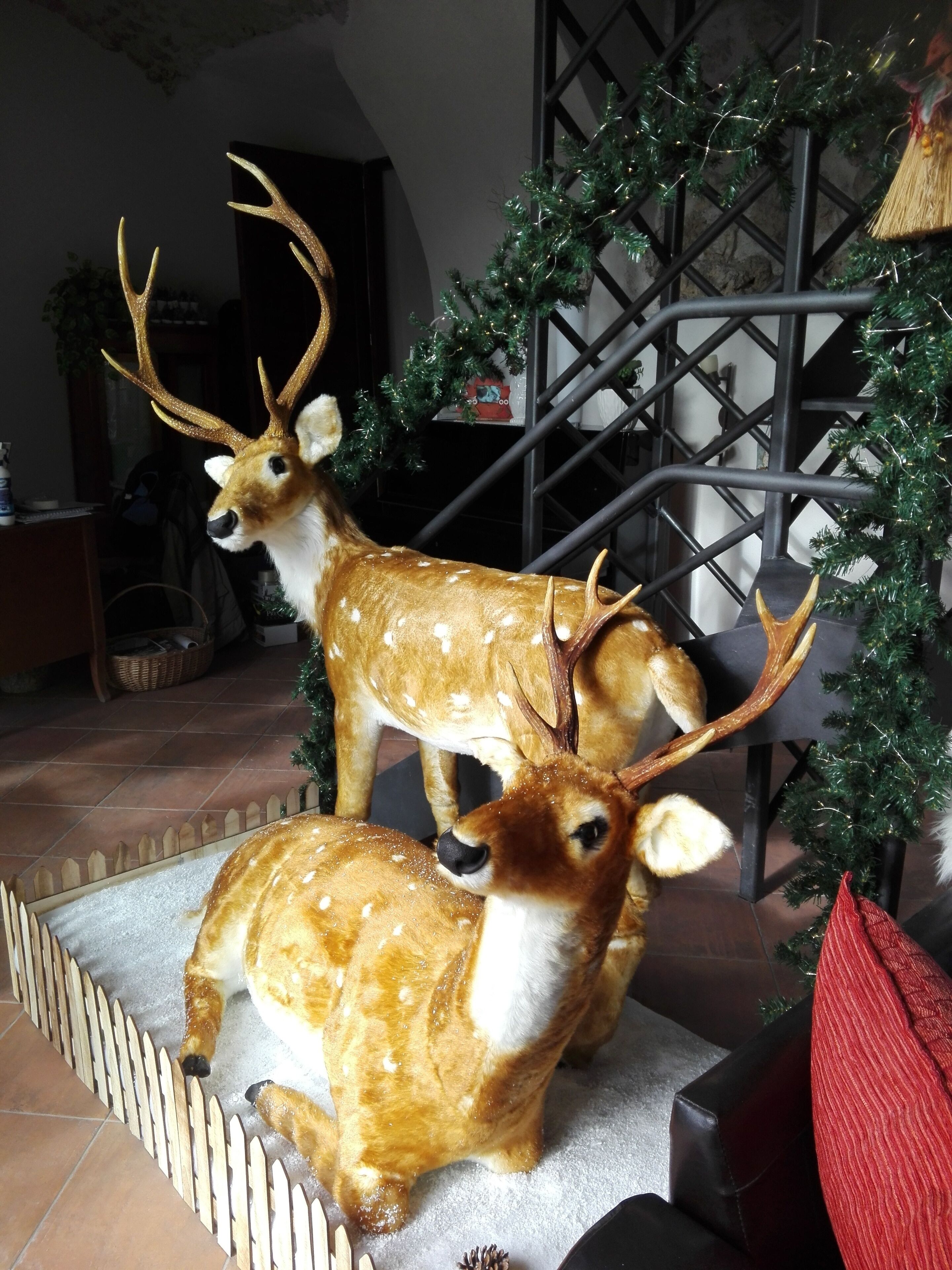 Zwei Hirschfiguren auf einer Plattform mit Zierzaun, umgeben von einem Weihnachtsbaum und einer Metallkonstruktion.