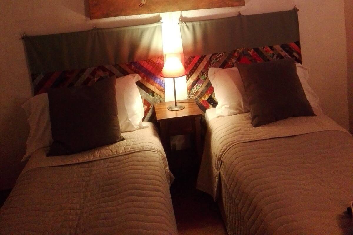 Une chambre avec deux lits, une lampe, un tableau représentant un hibou et une fenêtre avec des rideaux.