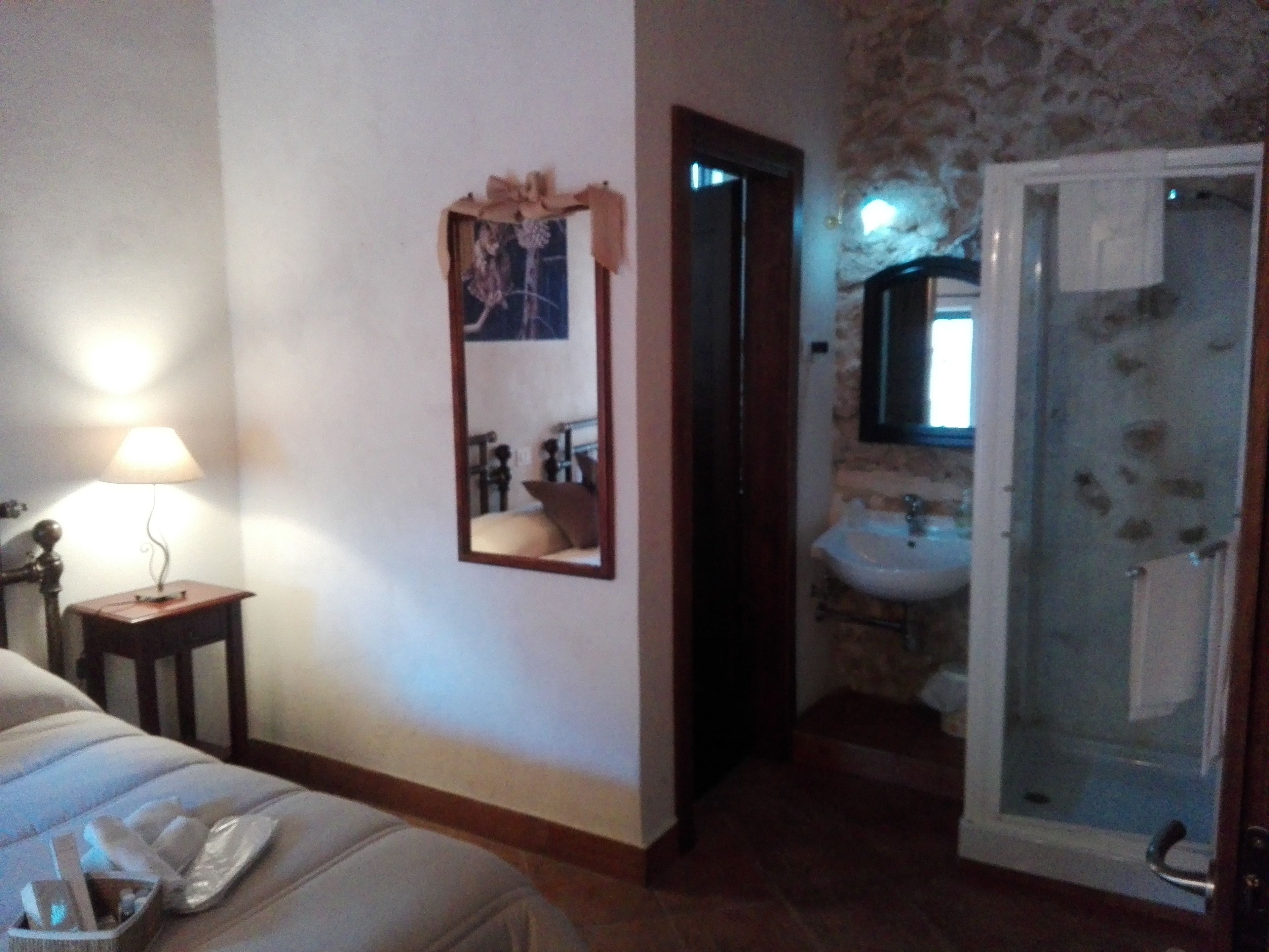 A bedroom with a bed, bedside table, lamp, and a mirror.