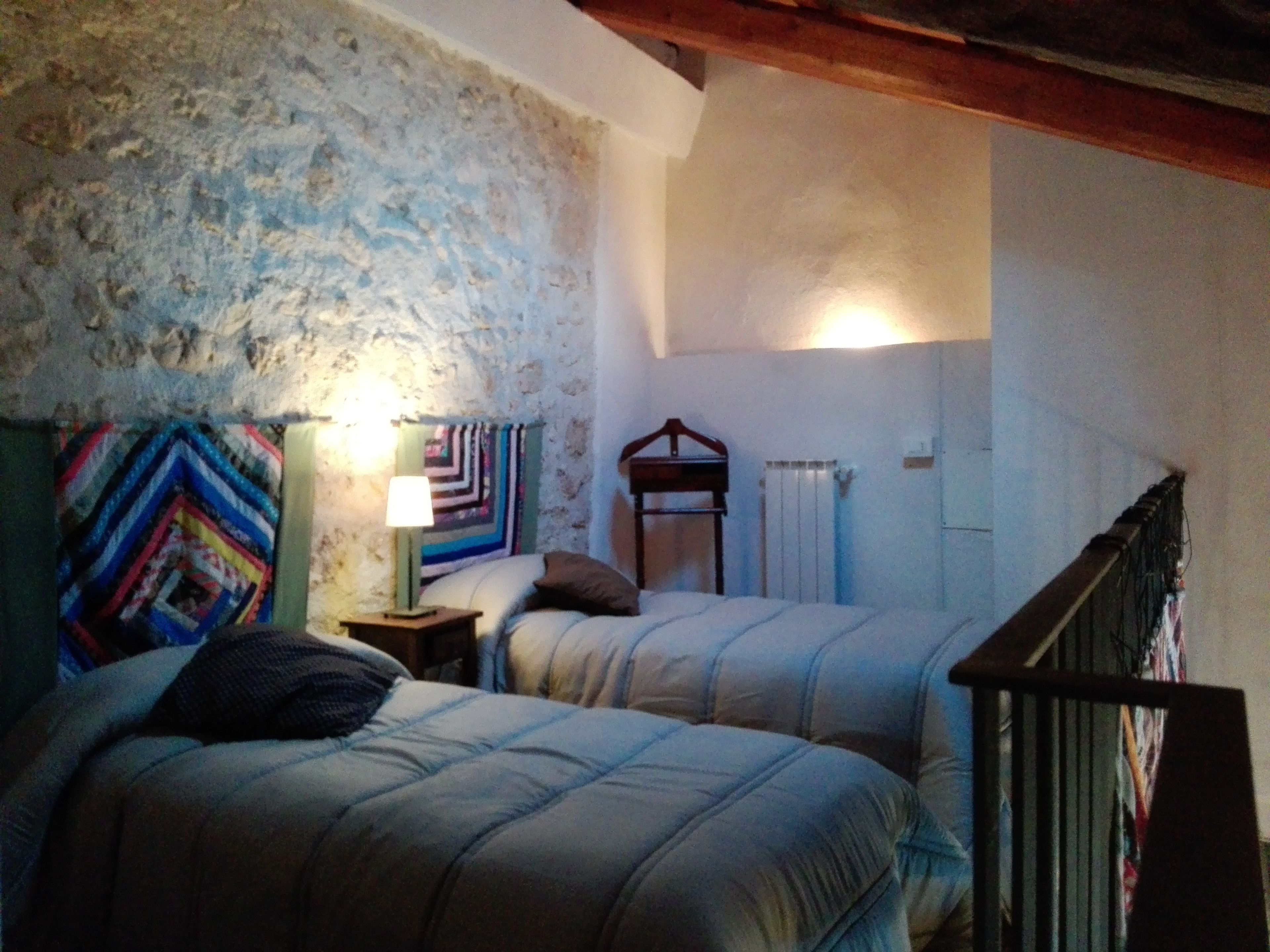 Une chambre avec deux lits, une table de chevet avec une lampe, une tête de lit en bois, un radiateur et un escalier.