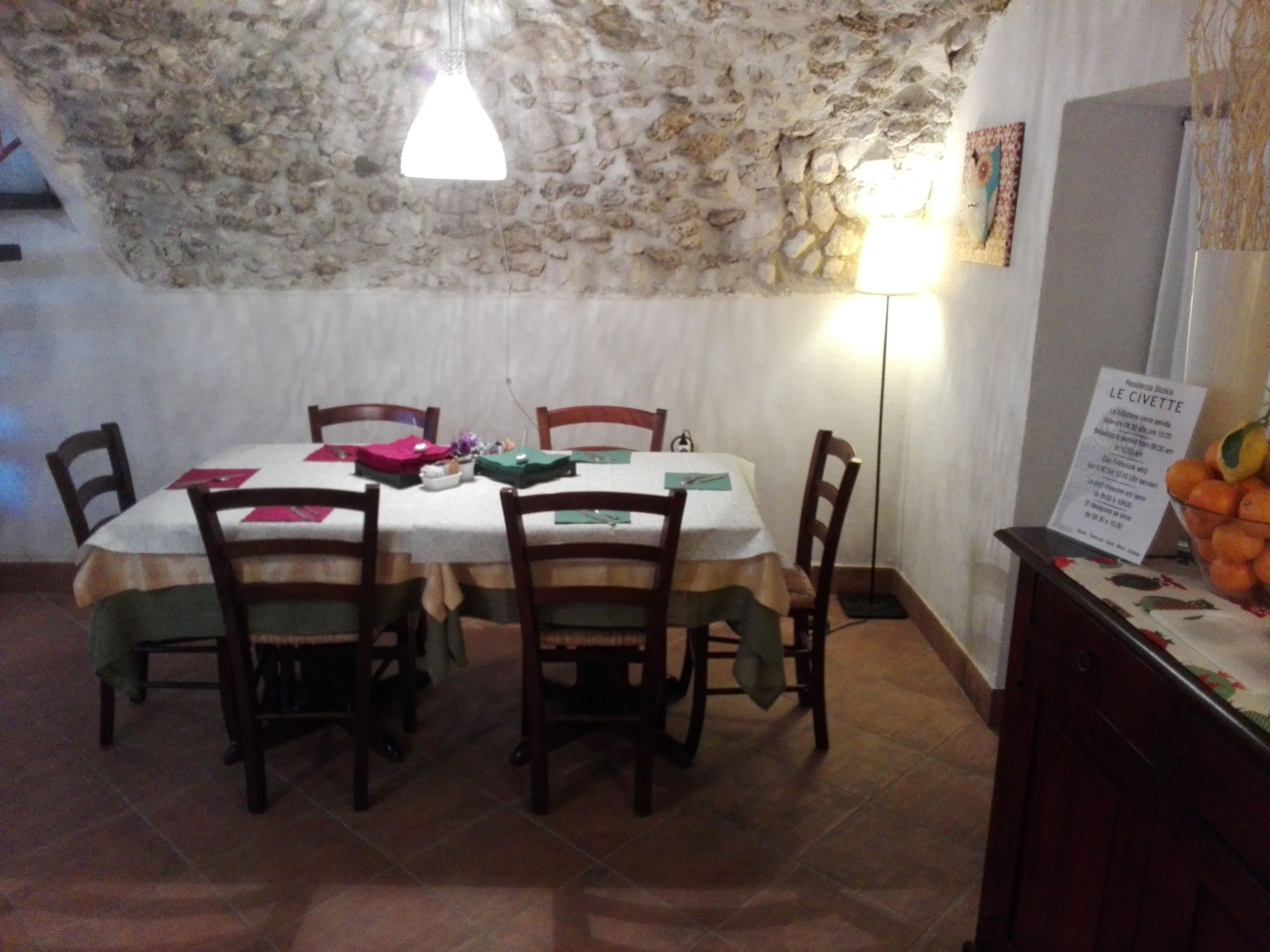 Comedor con pared de piedra, una mesa con sillas, una lámpara colgante y un menú en la pared.