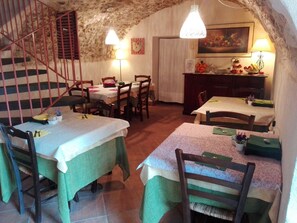Un comedor con mesas dispuestas para dos, una escalera con barandillas rojas y una pared de piedra rústica.