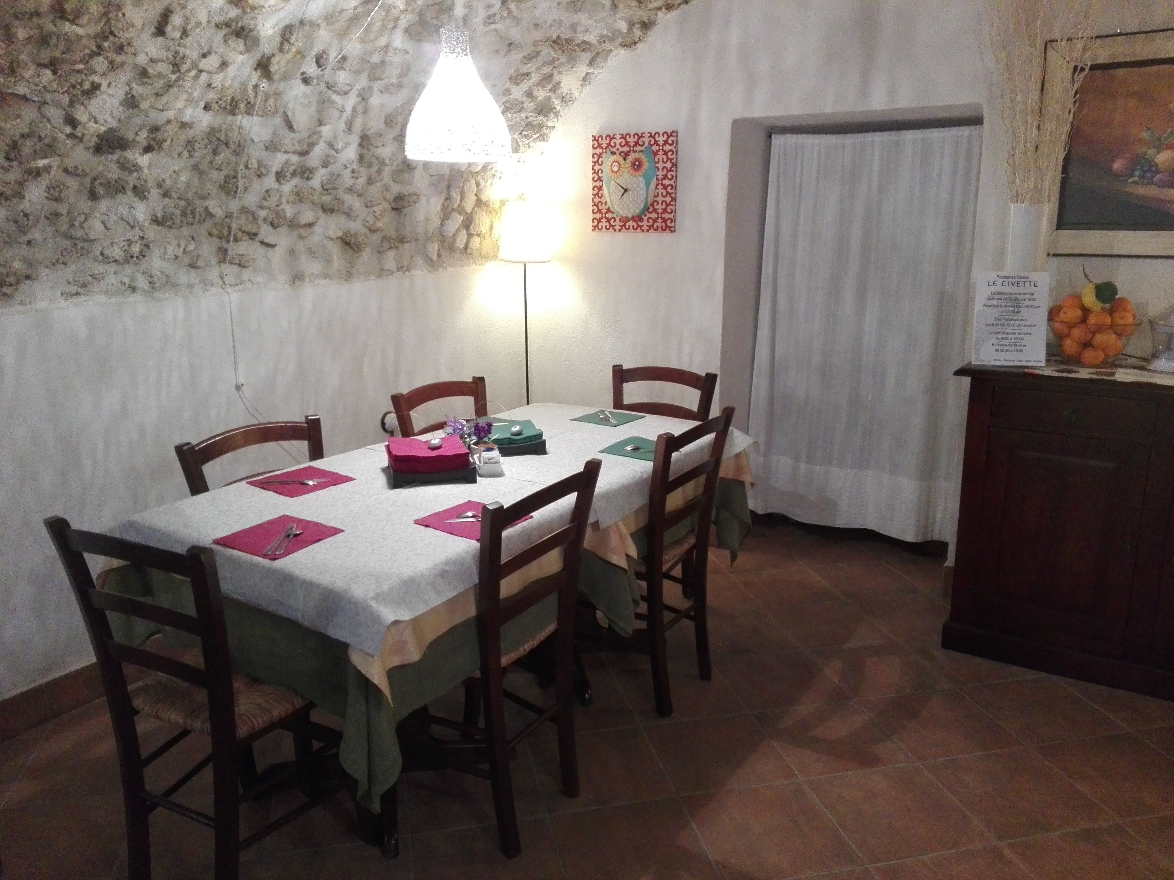 A dining area with a stone wall, a table set with chairs, a hanging light, and a fruit bowl on a cabinet.