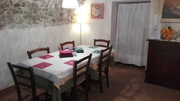 A dining area with a stone wall, a table set with chairs, a hanging light, and a fruit bowl on a cabinet.