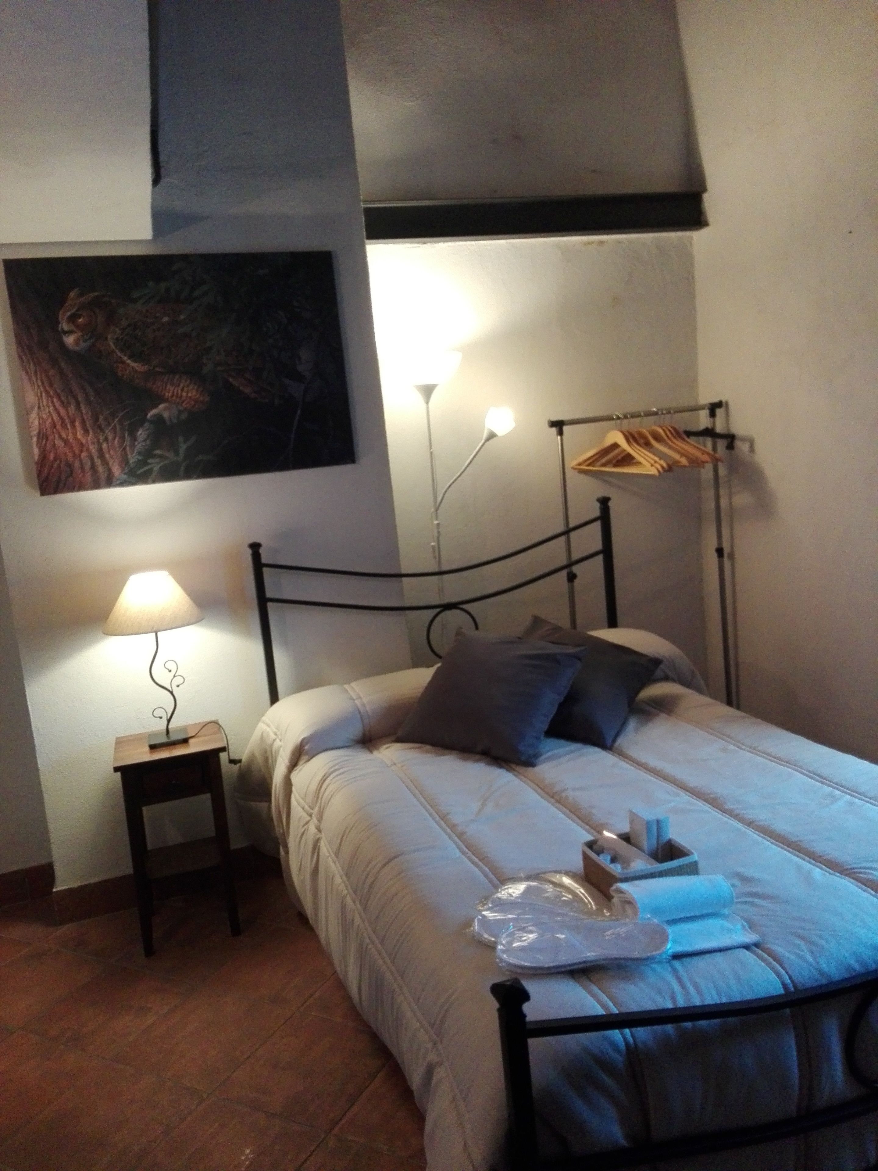 Camera da letto con un letto, comodino, lampada e una rastrelliera a parete con vestiti.