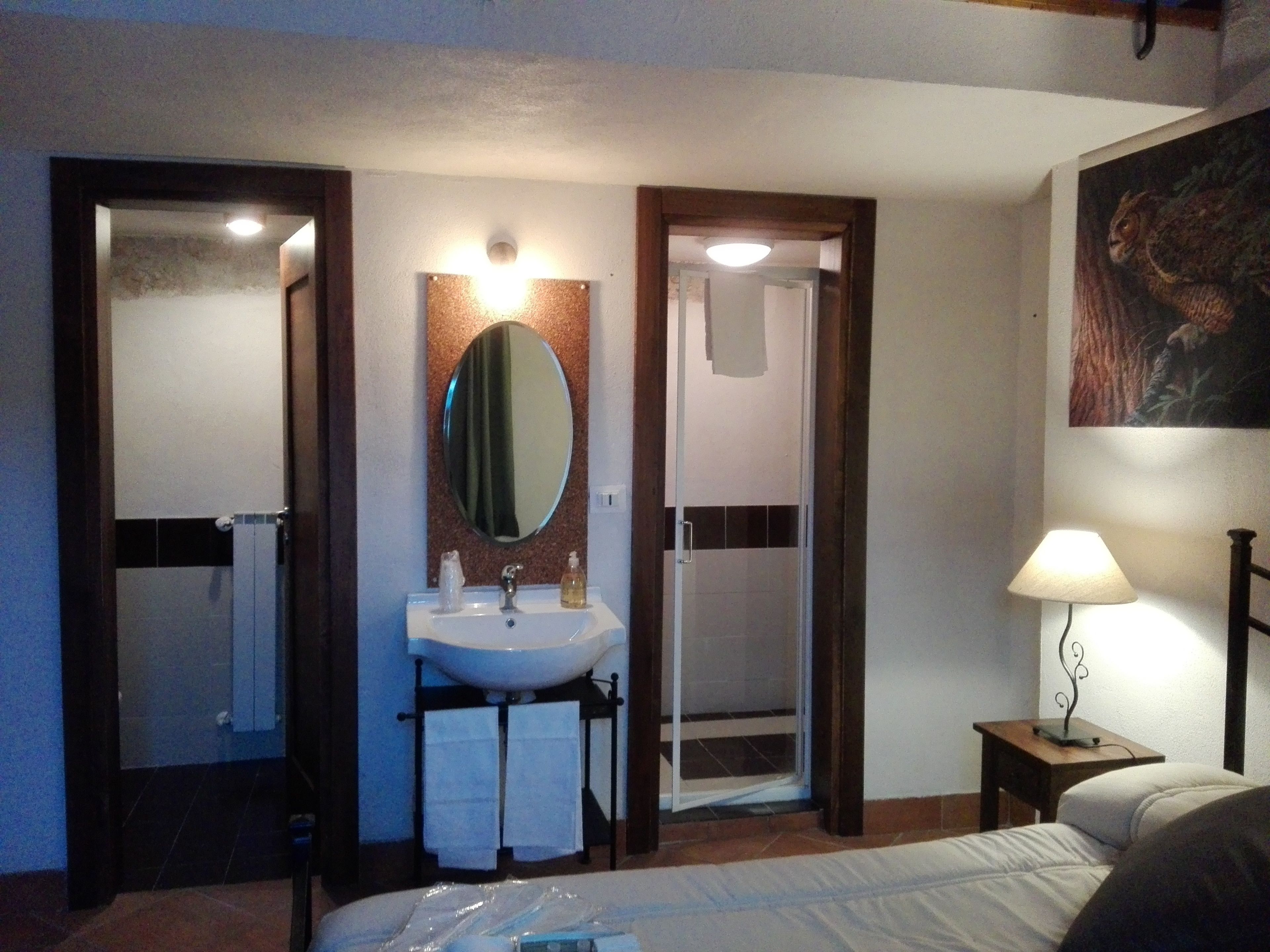 A hotel room with a bed, a bathroom with a sink and mirror, and a nightstand with a lamp.