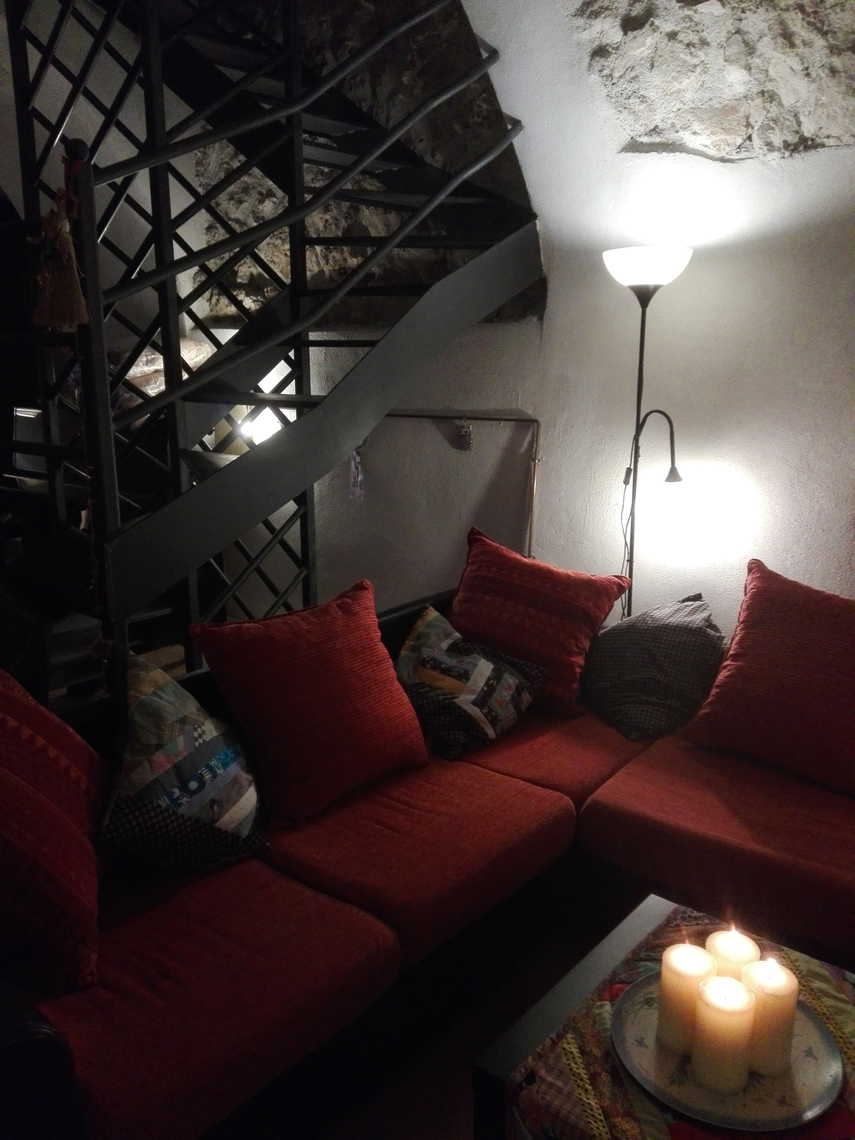Una habitación tenuemente iluminada con una escalera, un sofá rojo y una mesa con velas.