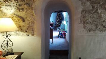 Un estrecho pasillo de piedra que conduce a una habitación con un árbol de Navidad, una lámpara y una mesa con mantel estampado.