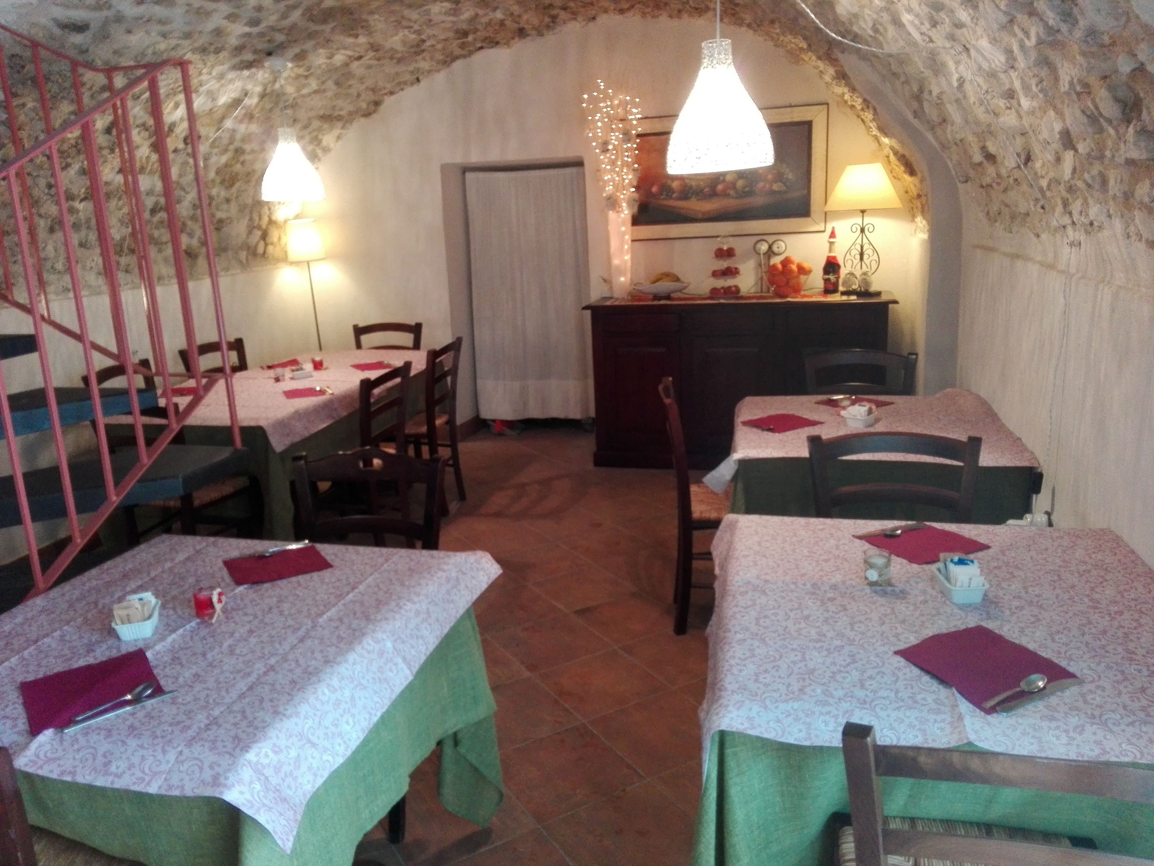 A rustic dining area with stone walls, wooden tables, and chairs. There are two pendant lights hanging above the tables.