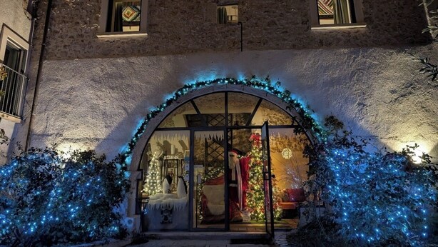 Une façade d’immeuble avec un revêtement extérieur en pierre, une entrée en verre et des décorations de Noël, notamment des guirlandes lumineuses et une figurine du Père Noël.