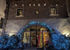 Een gevel van een gebouw met een stenen buitenkant, een glazen ingang en kerstversiering, waaronder lichtjes en een kerstmanbeeldje.