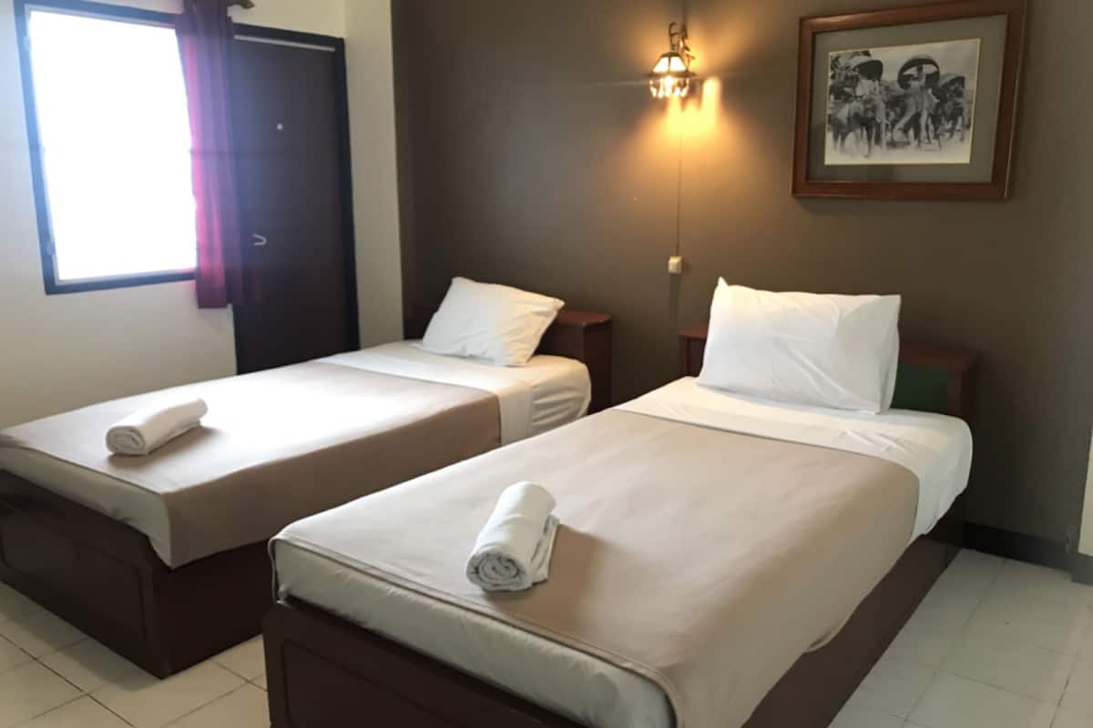 Hotelkamer met twee eenpersoonsbedden, elk voorzien van een opgerolde witte handdoek, een nachtkastje, een wandlamp en een ingelijst schilderij aan de muur.