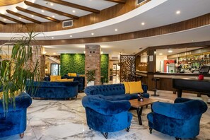 Un hall con sofás azules, una zona de bar y una pared verde.