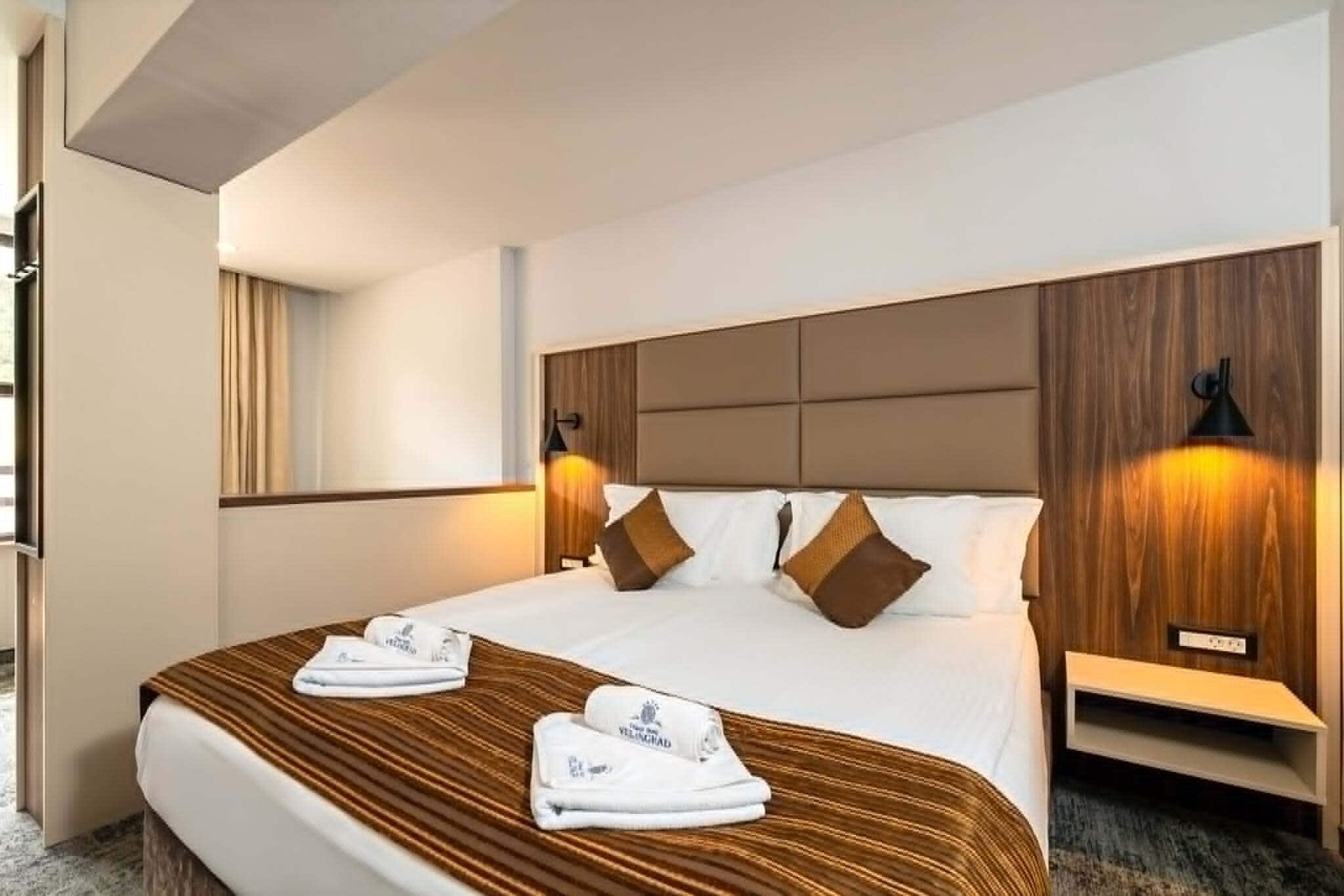 Une chambre d’hôtel avec un grand lit, deux tables de chevet, une tête de lit et une lampe fixée au mur.