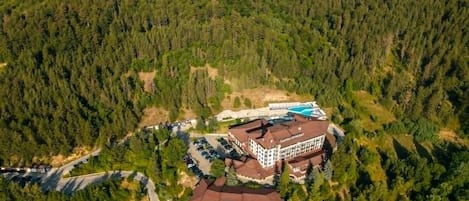 A lodge surrounded by dense forest, with a main building and a pool area.
