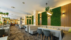 A restaurant with multiple dining booths and tables, green vertical gardens, and a patterned carpet. - Grand Hotel Velingrad (Velingrad)