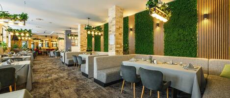 Un restaurante con varios reservados y mesas, jardines verticales verdes y una alfombra estampada.