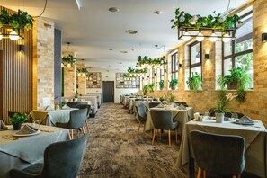 A restaurant with multiple tables, chairs, and potted plants. - Grand Hotel Velingrad (Velingrad)