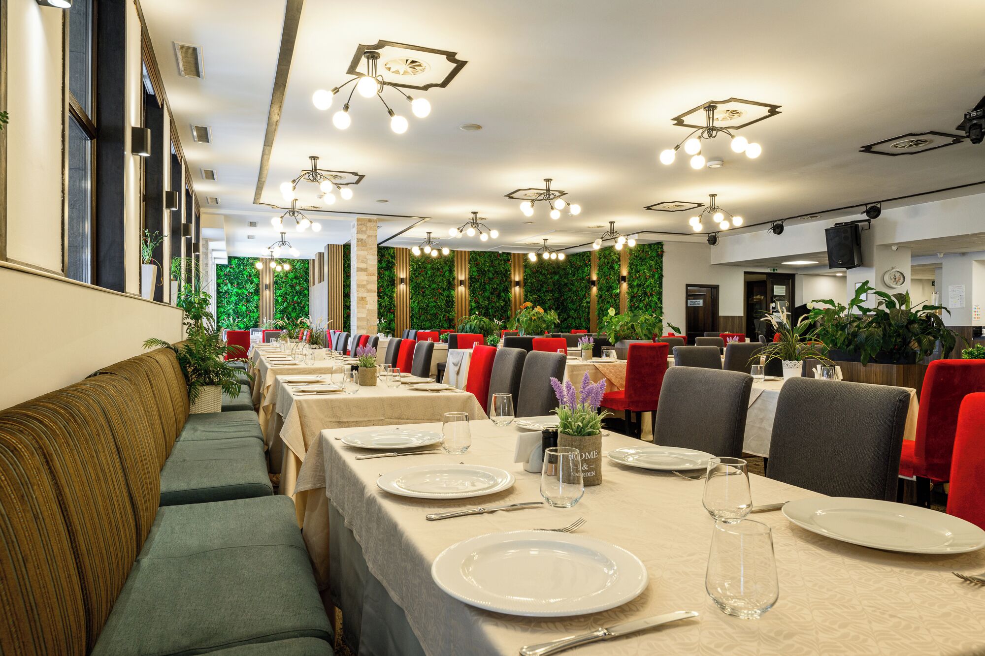 Un restaurant avec de longues tables, des chaises rouges et grises, et des jardins verticaux.