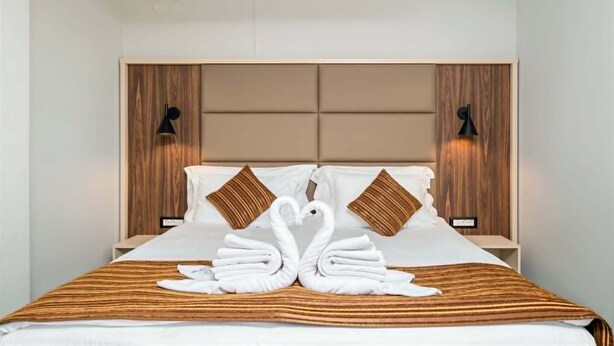 A hotel room with a bed, headboard, bedside lamps, and a decorative swan towel arrangement. - Grand Hotel Velingrad (Velingrad)