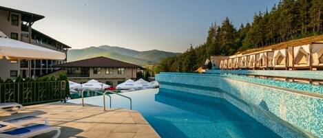 Una piscina con sillas de descanso y un edificio con vista a las montañas.