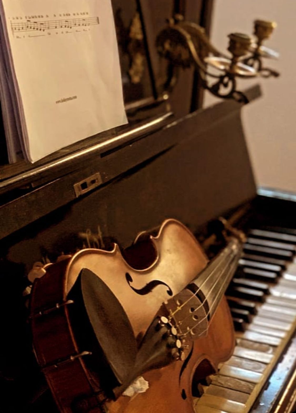 Un violín apoyado contra un piano, con partituras encima.