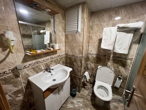 A bathroom with a sink, toilet, and mirror. There are towels hanging on the wall and a shelf with toiletries. - Hotel Cenka Ephesus (Selçuk)