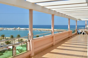 A balcony with a view of the sea, a covered area with chairs, and a railing.