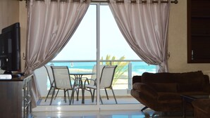 Una habitación con balcón y vistas a la playa, un sofá marrón, un televisor y una mesa de comedor con sillas.