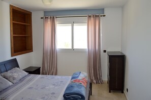 A bedroom with a bed, a nightstand, a dresser, and a window with curtains.