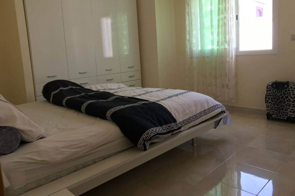 A bedroom with a bed, a wardrobe, a window with curtains, and a leopard print suitcase.