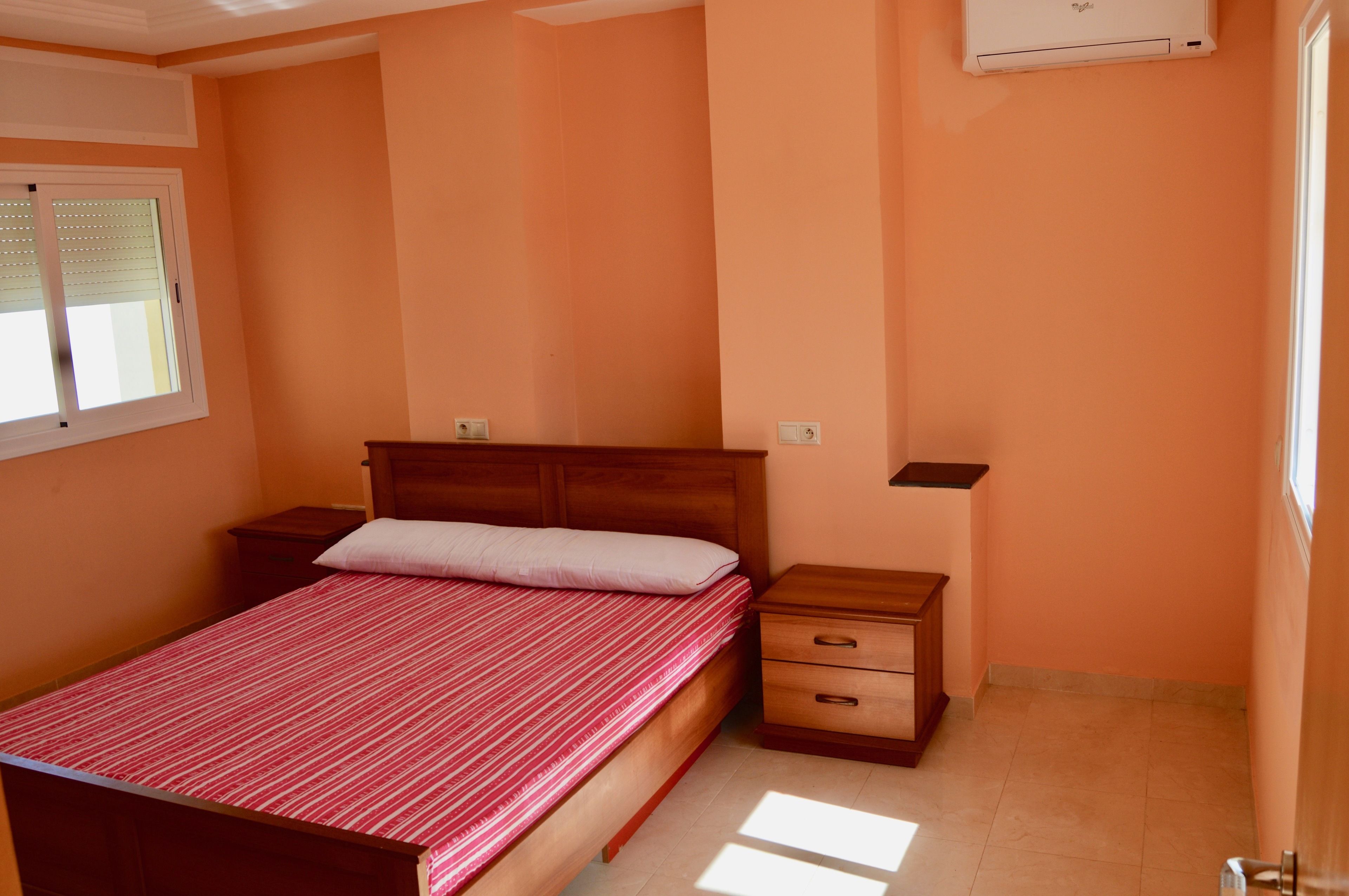 A bedroom with a single bed, a nightstand, a drawer, and a window with blinds.