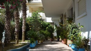 Un pasillo exterior cubierto con plantas en macetas y palmeras.