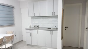 A compact kitchen with white cabinets, a sink, and a dining area with a table and chairs. - Comfort Apartments (Haifa)