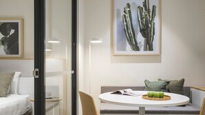 A modern room with a bed, a glass partition, a round table with chairs, a sofa, and a cactus painting on the wall. - Quest Epping (Epping)