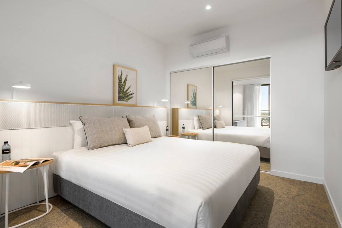 Quarto de hotel com uma cama grande, mesas de cabeceira, um espelho e um aparelho de ar condicionado.