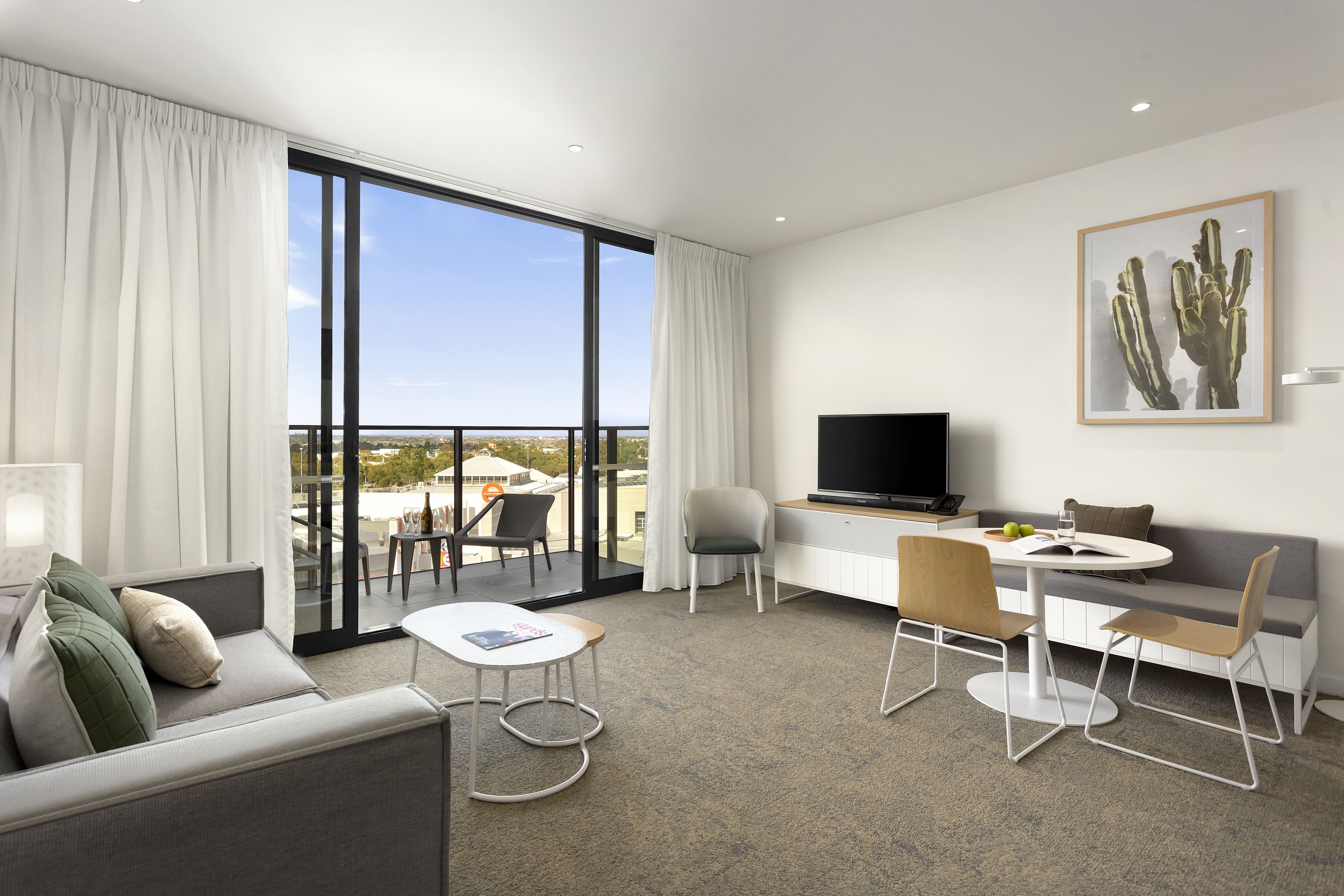 Une chambre d’hôtel moderne dotée d’un balcon, d’une télévision à écran plat, d’un coin repas et d’un espace salon.