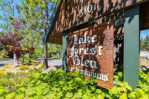 A wooden sign with "Lake Forest Glen" and "Condominium" written on it, set against a backdrop of trees and greenery.