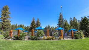 A well-maintained outdoor area with a pool, surrounded by a fence and blue umbrellas, set against a backdrop of tall trees.