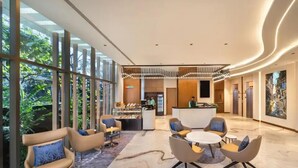 Een moderne lobby met een receptiebalie, een zithoek en grote ramen met uitzicht op groen.