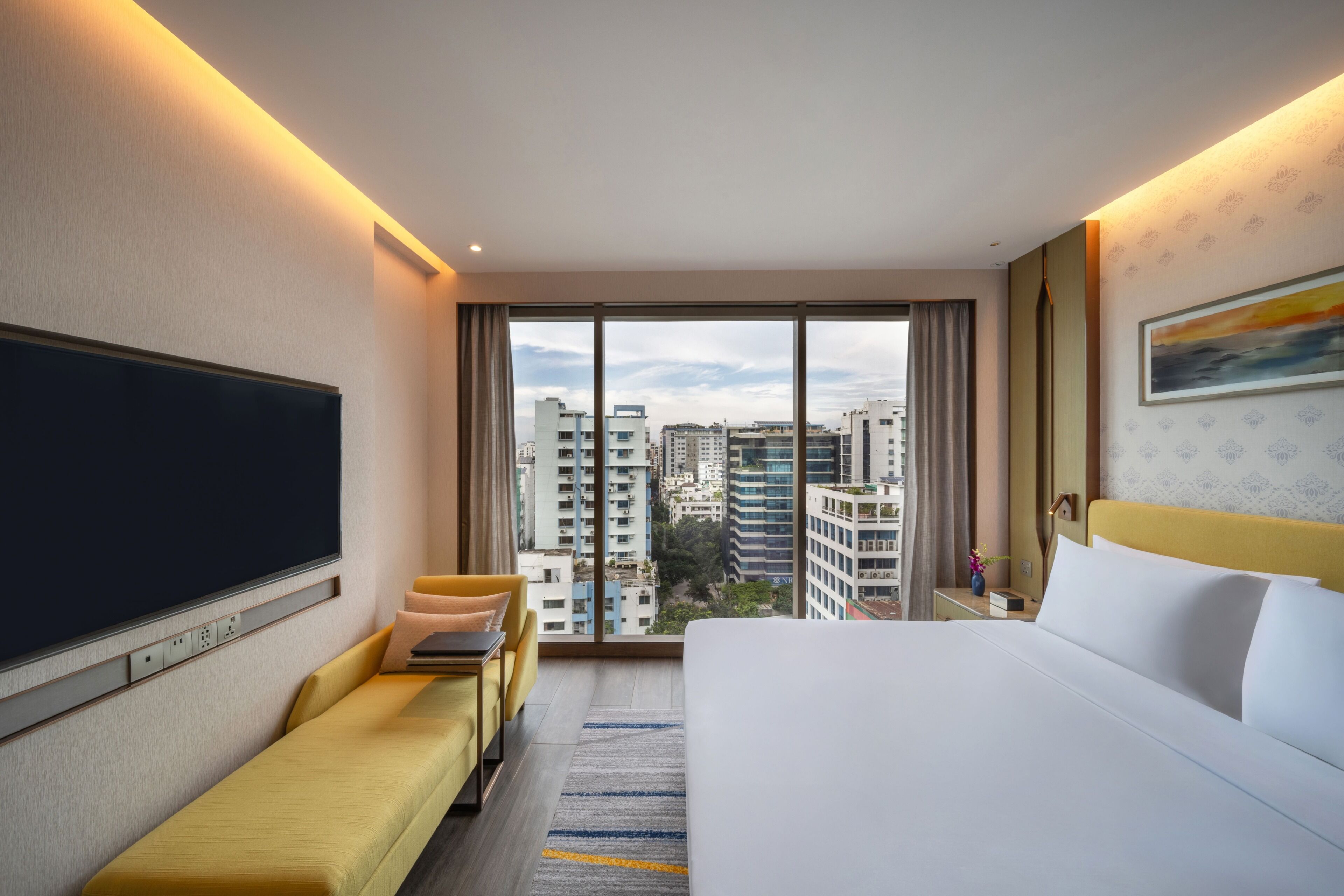 Quarto de hotel com cama grande, sofá, televisão e vista para a paisagem urbana.