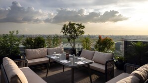 Een terras op het dak met een eettafel gedekt voor twee personen, omringd door zachte zitplaatsen en een uitzicht op de stad.