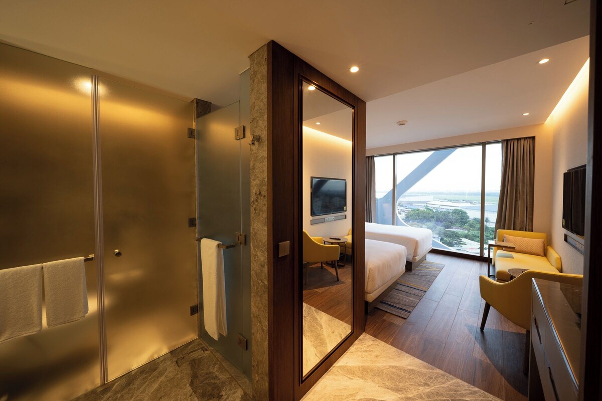 A modern hotel room with a large bed, a TV, a desk, and a view of the city.
