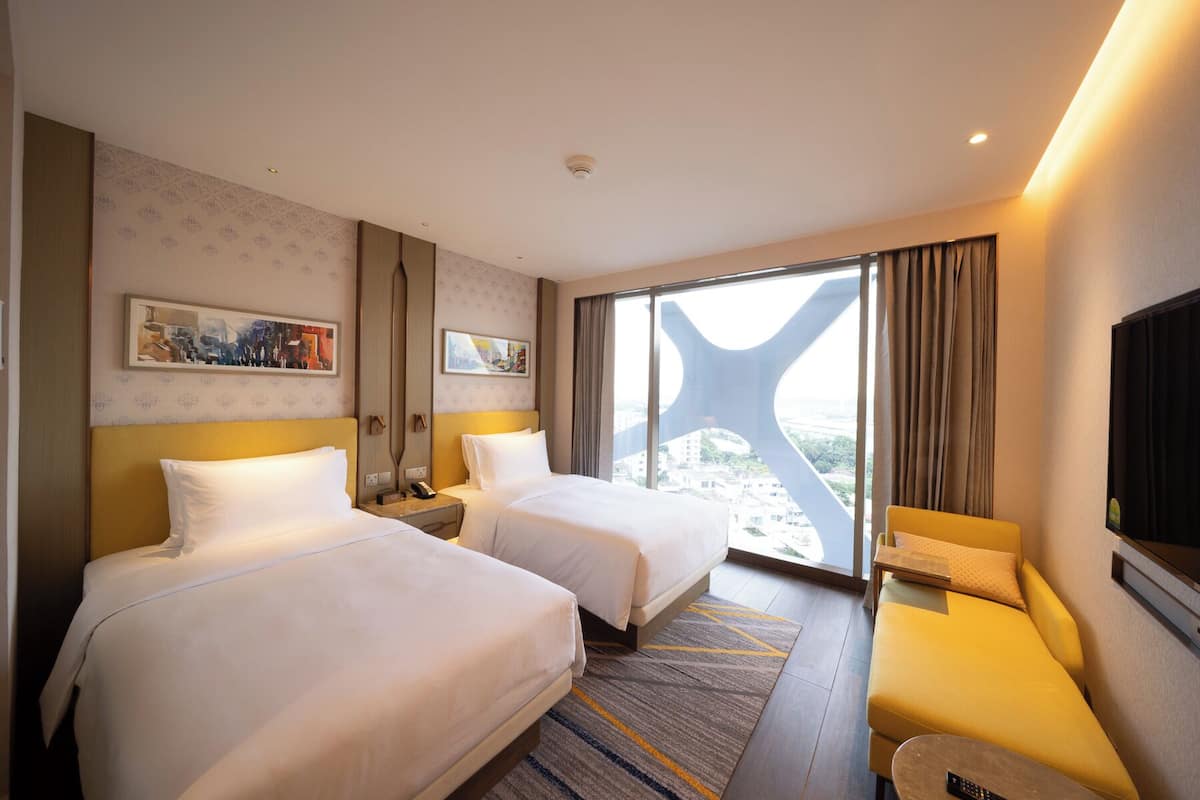 A hotel room with two beds, a sofa, a TV, and a large window with a view.