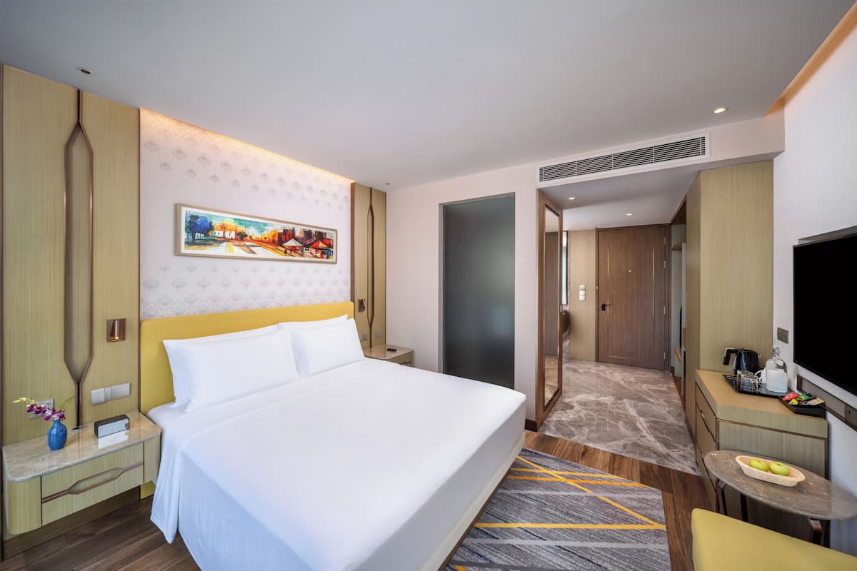 A hotel room with a large bed, a TV, a desk, and a chair.