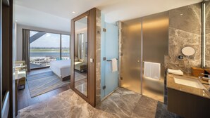 Een moderne hotelkamer met een groot bed, een badkamer met een marmeren aanrechtblad en uitzicht op de stad door een groot raam.
