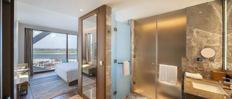 Una habitación de hotel moderna con una cama grande, un baño con encimera de mármol y vistas a la ciudad a través de un ventanal amplio.