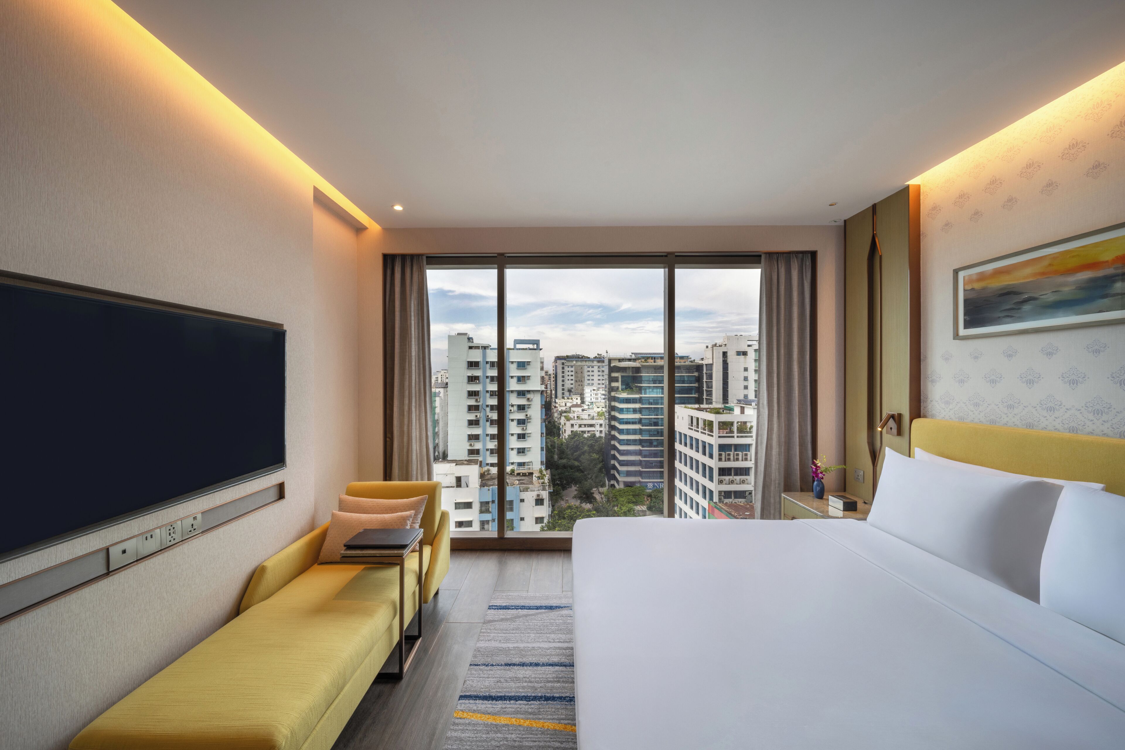A hotel room with a large bed, a sofa, a TV, and a city view.