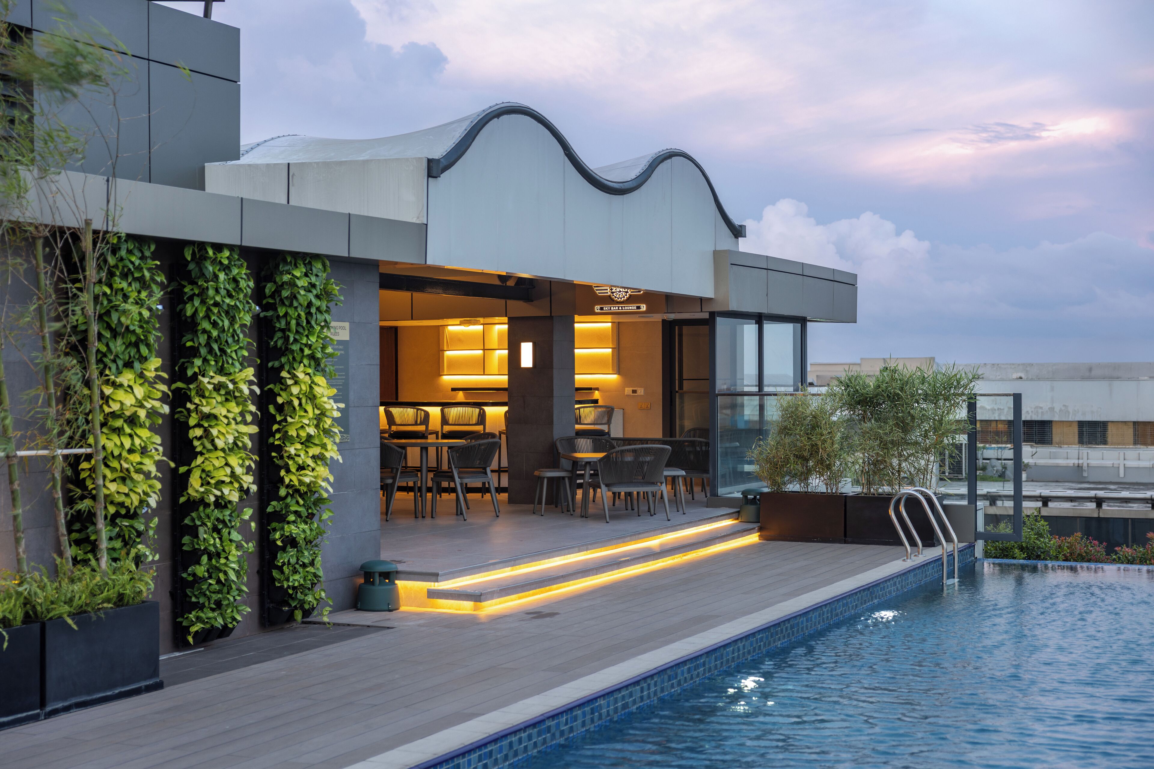 Un edificio moderno con piscina, mobiliario exterior y jardines verticales.